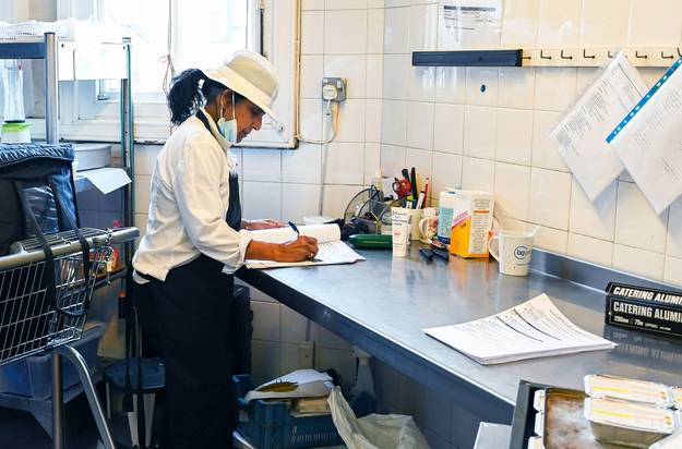 Food-service worker checking a laminated cleaning timetable in a commercial kitchen